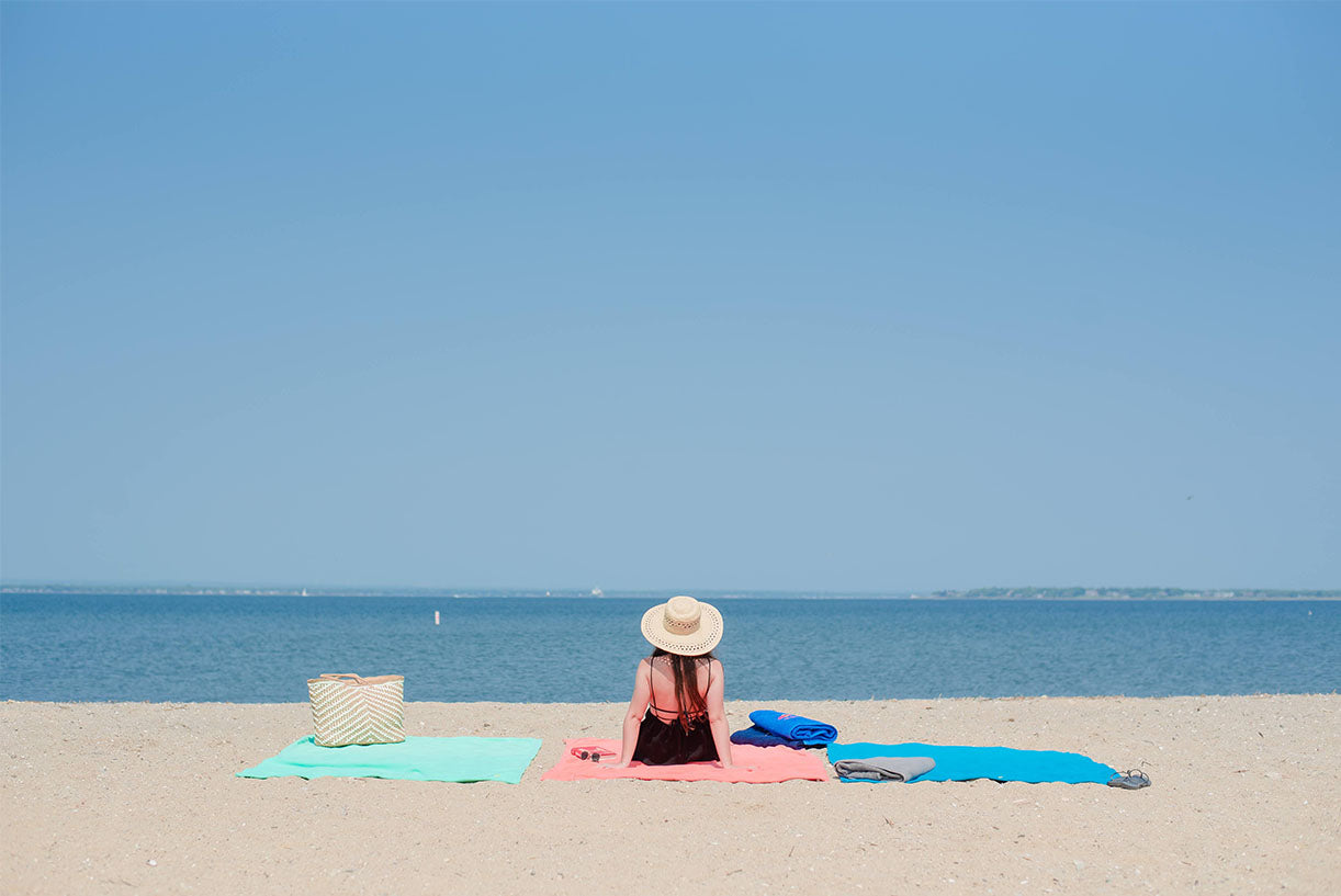 Women sitting up watching the ocean on a Coral Peaceful Touch fleece blanket made by American Blanket Company