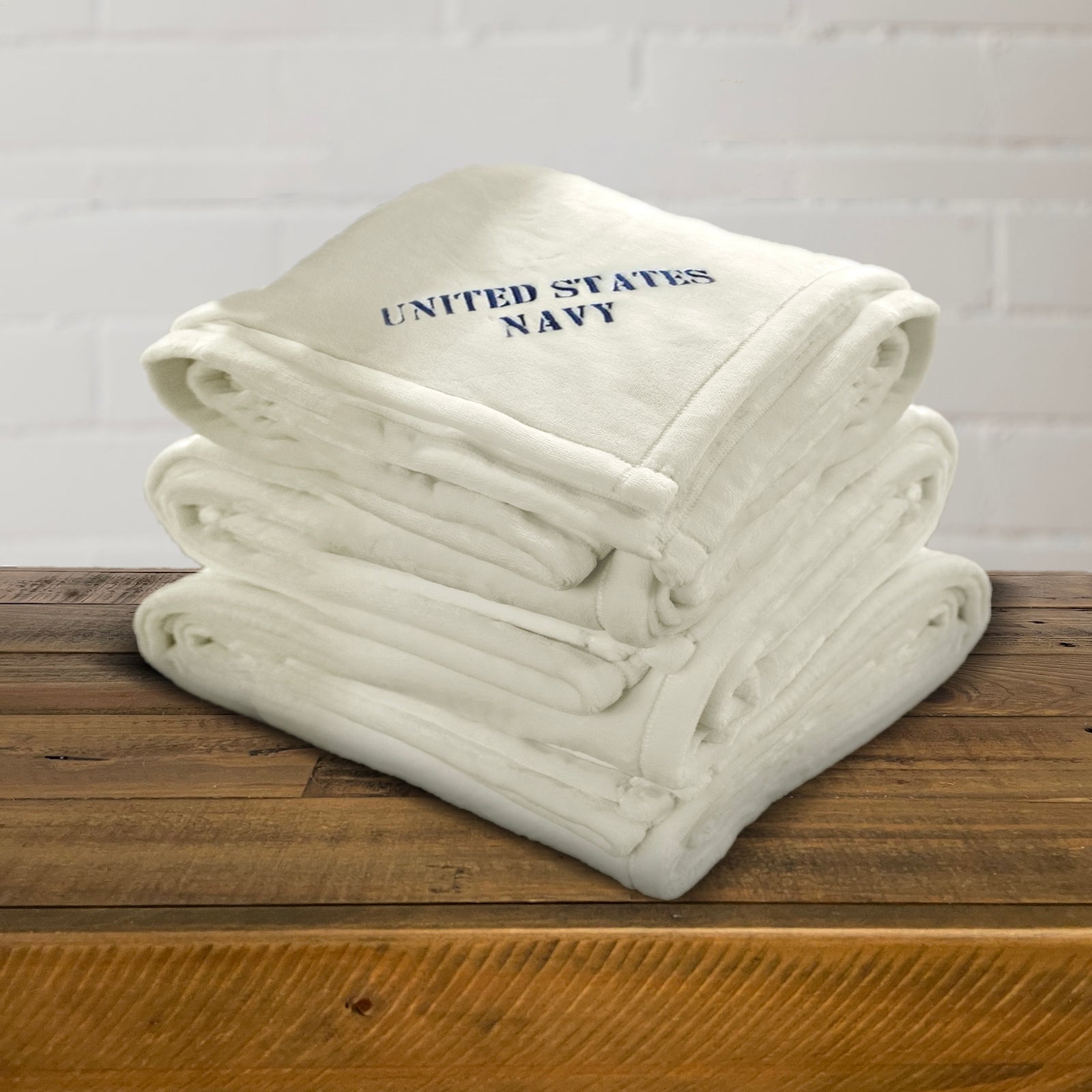 American Blanket Company - Luster Loft fleece Blanket - military fleece blanket stack on a wooden chest against a white brick background
