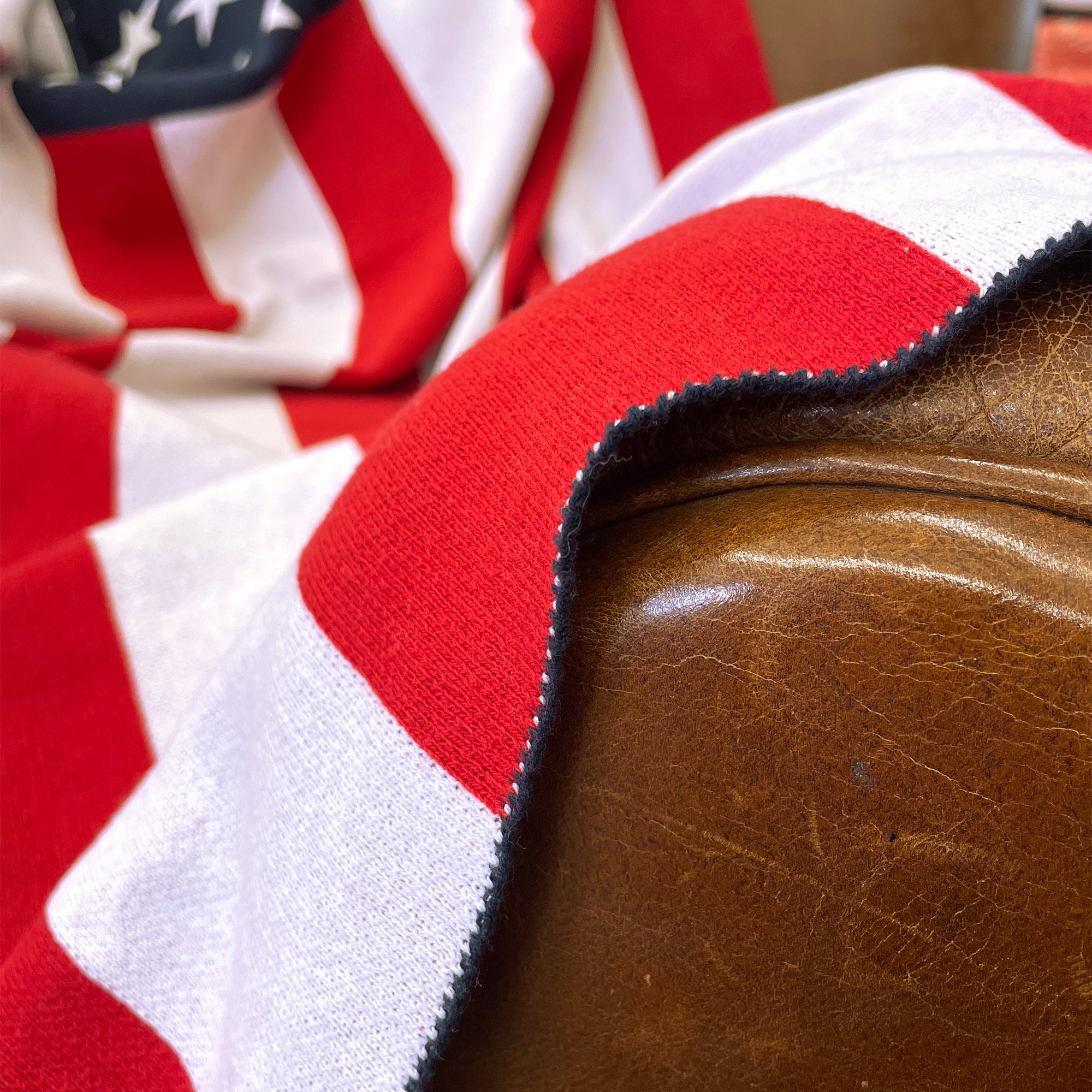 AMERICAN BLANKET COMPANY - KNITTED FLAG BLANKETS - Close up of blue stitched edge on a light brown leather armchair. 50% Cotton 50% polyester