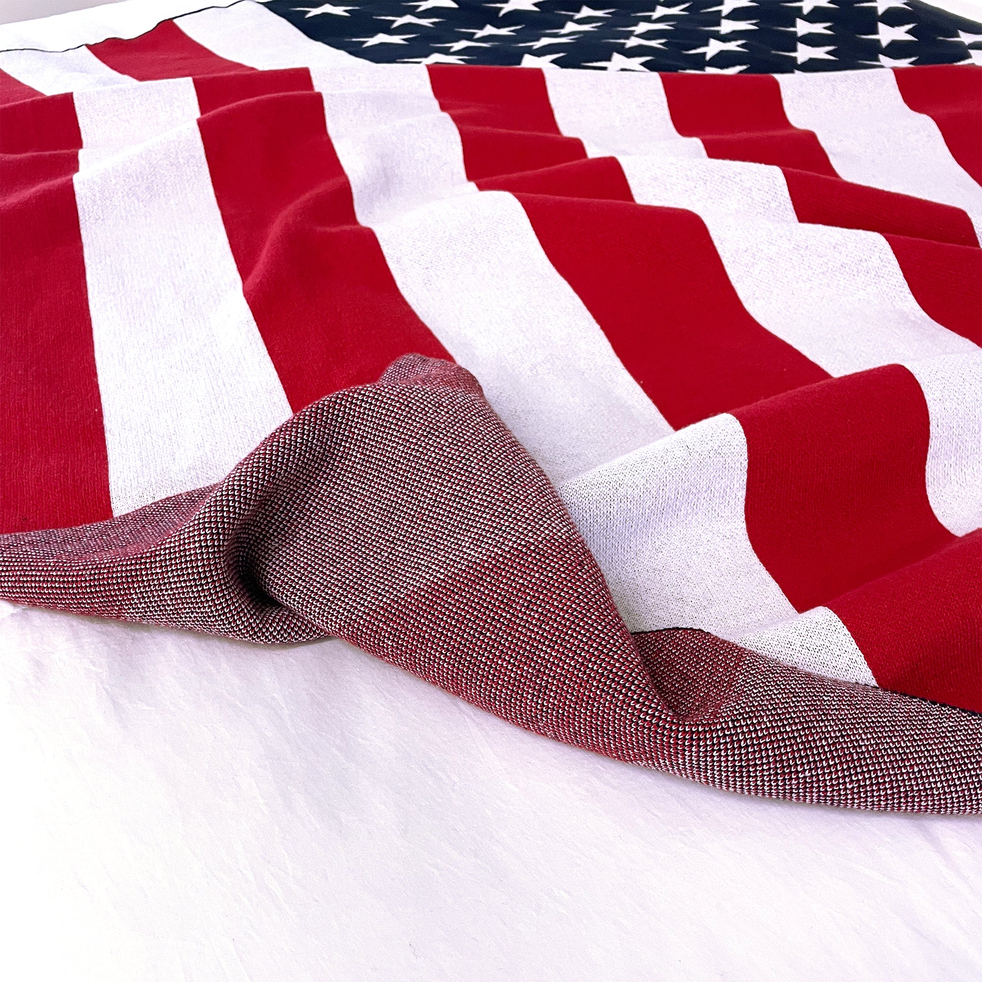 AMERICAN BLANKET COMPANY - KNITTED FLAG BLANKETS - Flag Blanket on white cotton bedsheet foled over showing the reverse side of the knitted blanket. 50% Cotton 50% polyester
