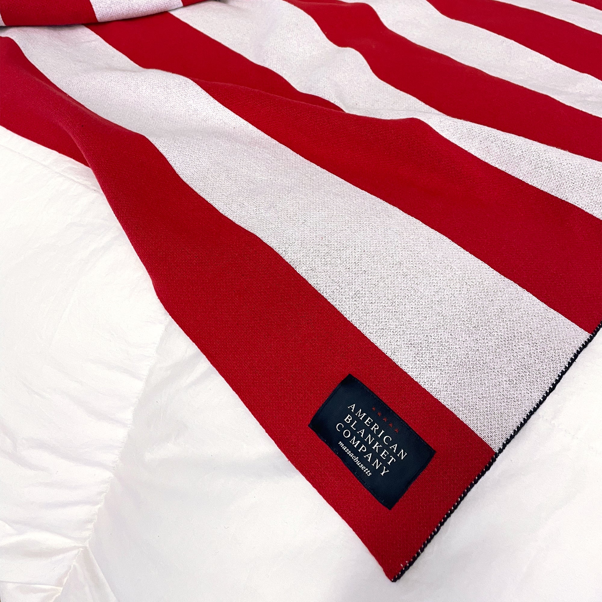 AMERICAN BLANKET COMPANY - KNITTED FLAG BLANKETS - Flag blanket on corner of bed on a heavyweight comforter showing the corner sew in tag with the american blanket company logo. 50% Cotton 50% polyester