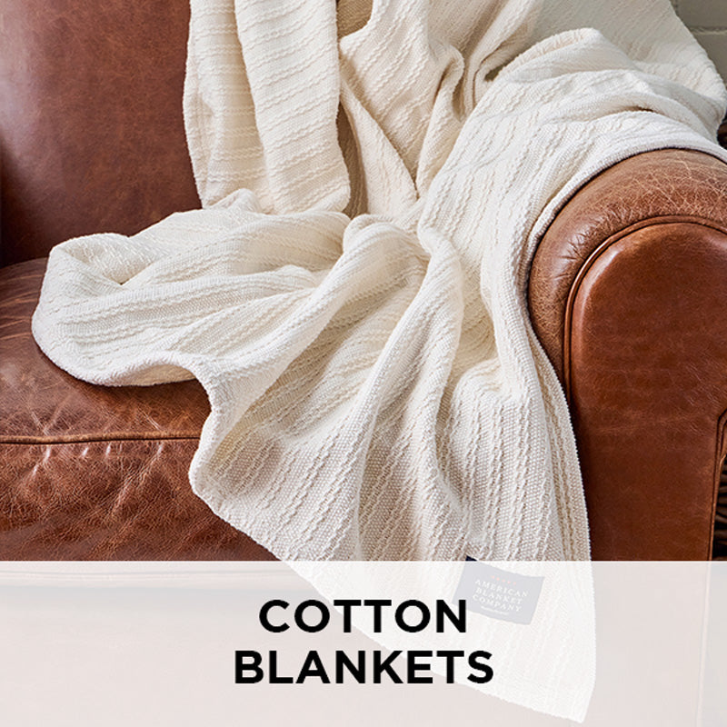 AMERICAN BLANKET COMPANY - CABLE WEAVE 100% COTTON BLANKET - A 100% COTTON BLANKET DRAPED OVER A LIGHT LEATHER VINTAGE ARMCHAIR