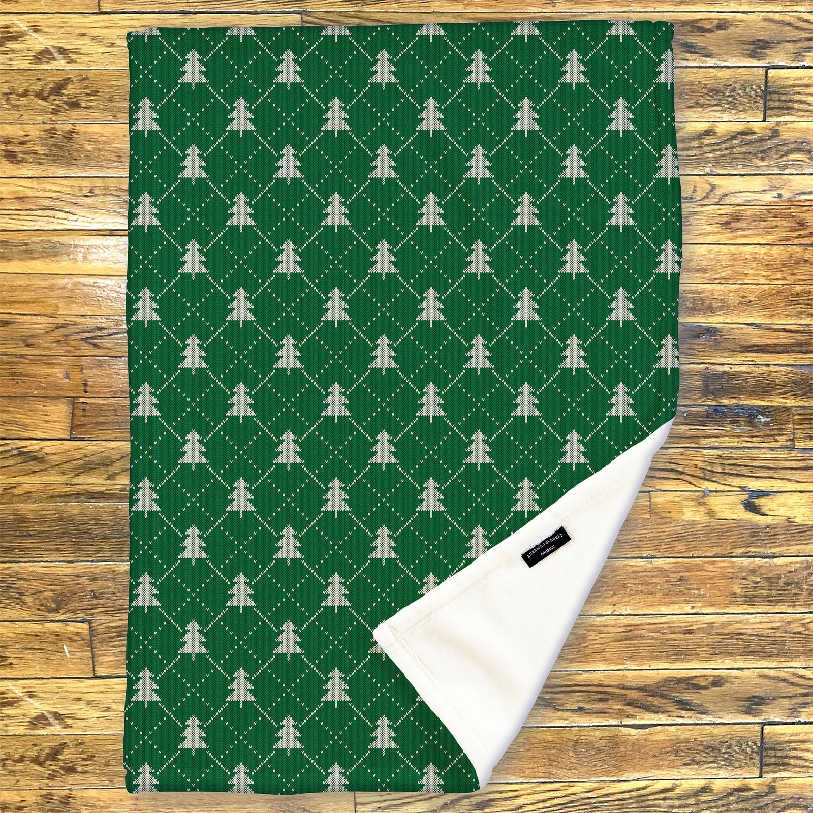 American Blanket Company - Luster Loft Fleece Blanket - Printed Holiday Throw Blanket - Green fleece blanket with tree pattern on a wooden surface