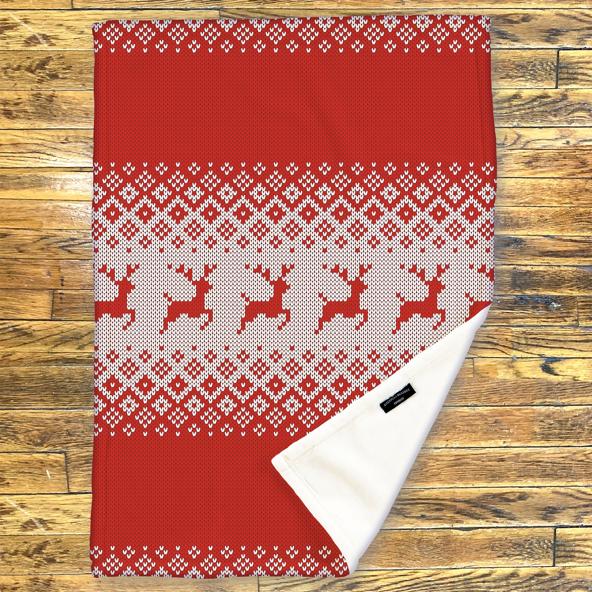 American Blanket Company - Luster Loft Fleece Blanket - Printed Holiday Throw Blanket - Red and white patterned fleece blanket with reindeer design on a wooden surface