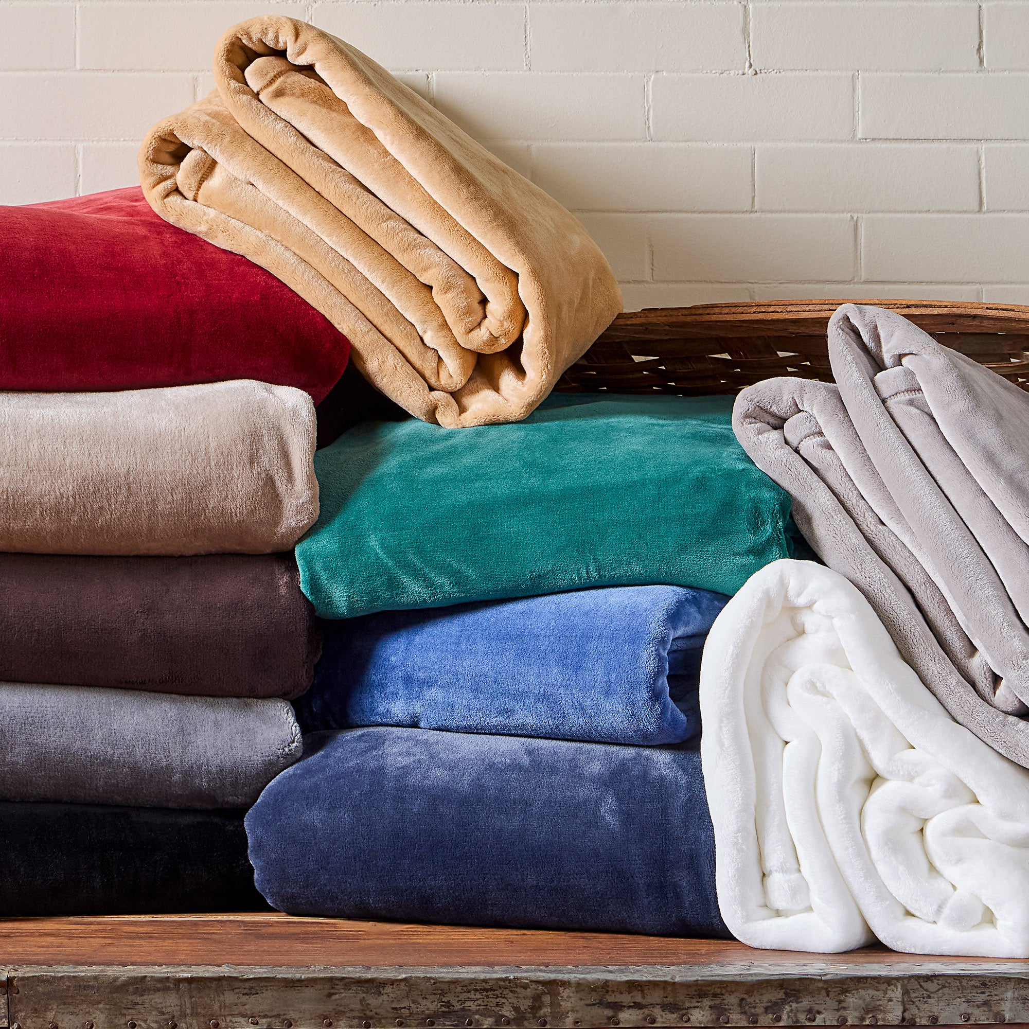 American blanket company - luster loft Fleece Blankets - Stack of colorful folded blankets on a wooden surface with a white brick wall background.