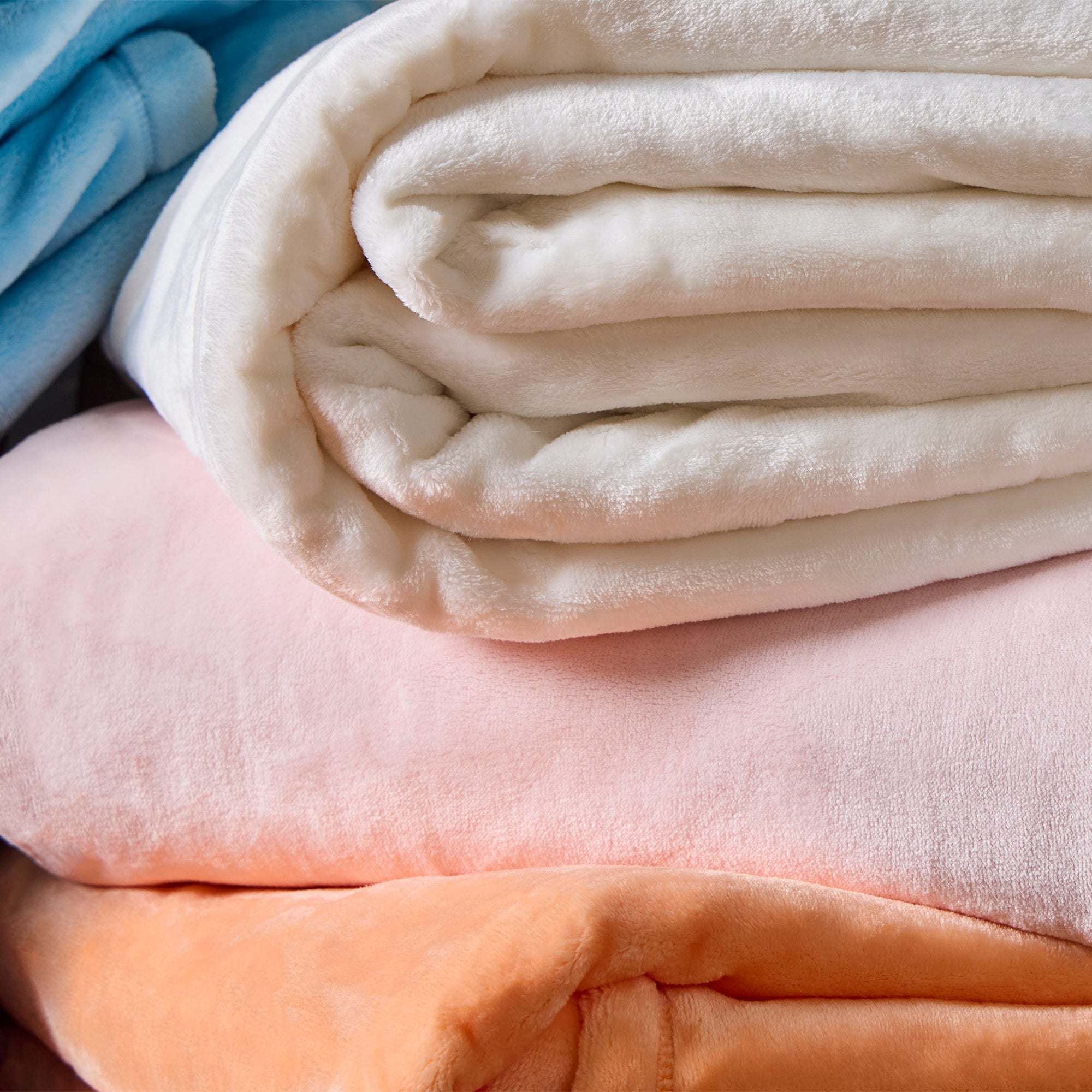 American Blanket Company - Luster Loft Fleece Oversized Fleece Blankets -  Stack of folded blankets in white, pink, blue, and orange 