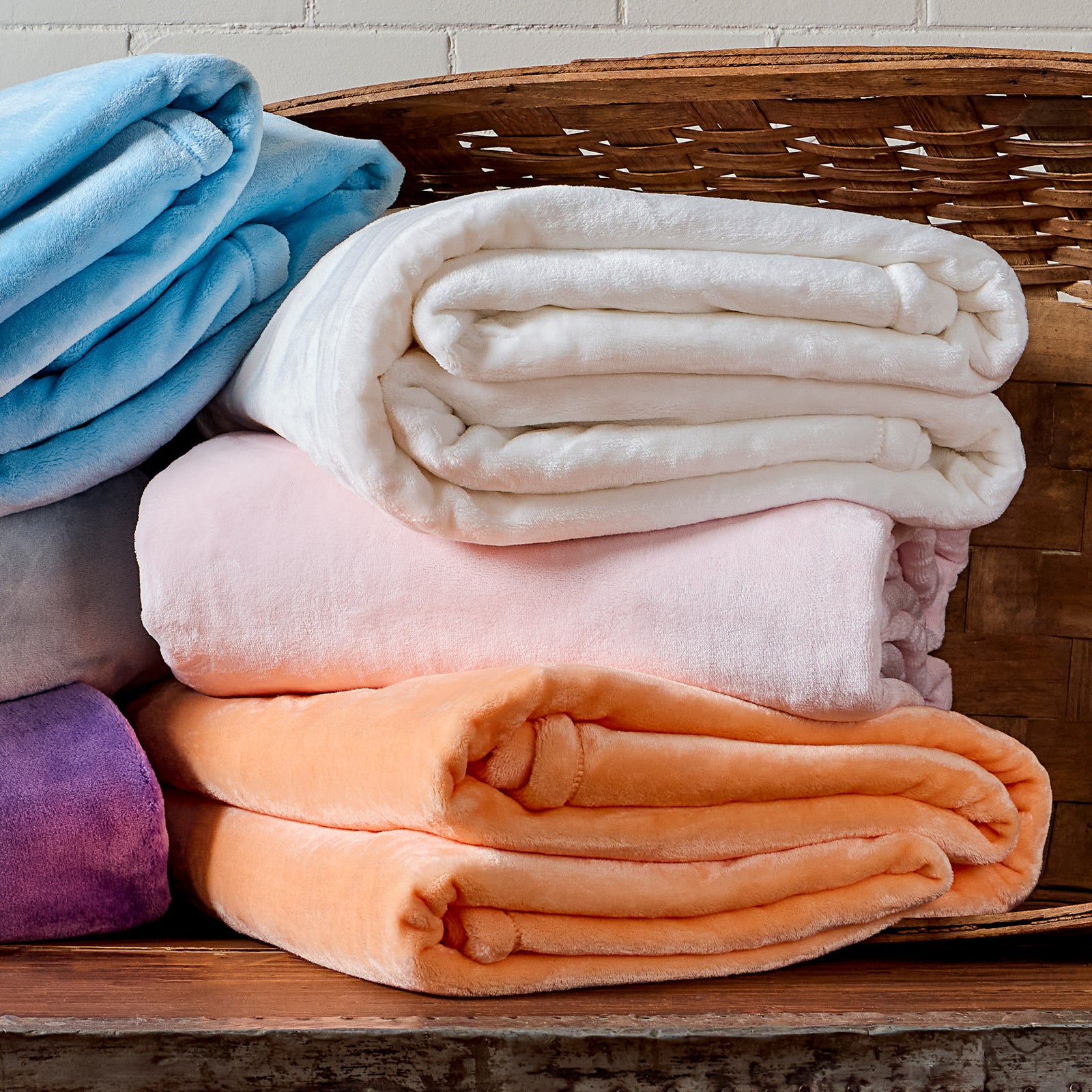 AMERICAN BLANKET COMPANY - LUSTER LOFT FLEECE BLANKETS - COLORFUL STACKS OF LUSTER LOFT  FLEECE BLANKETS FALLING OUT OF A BASKET