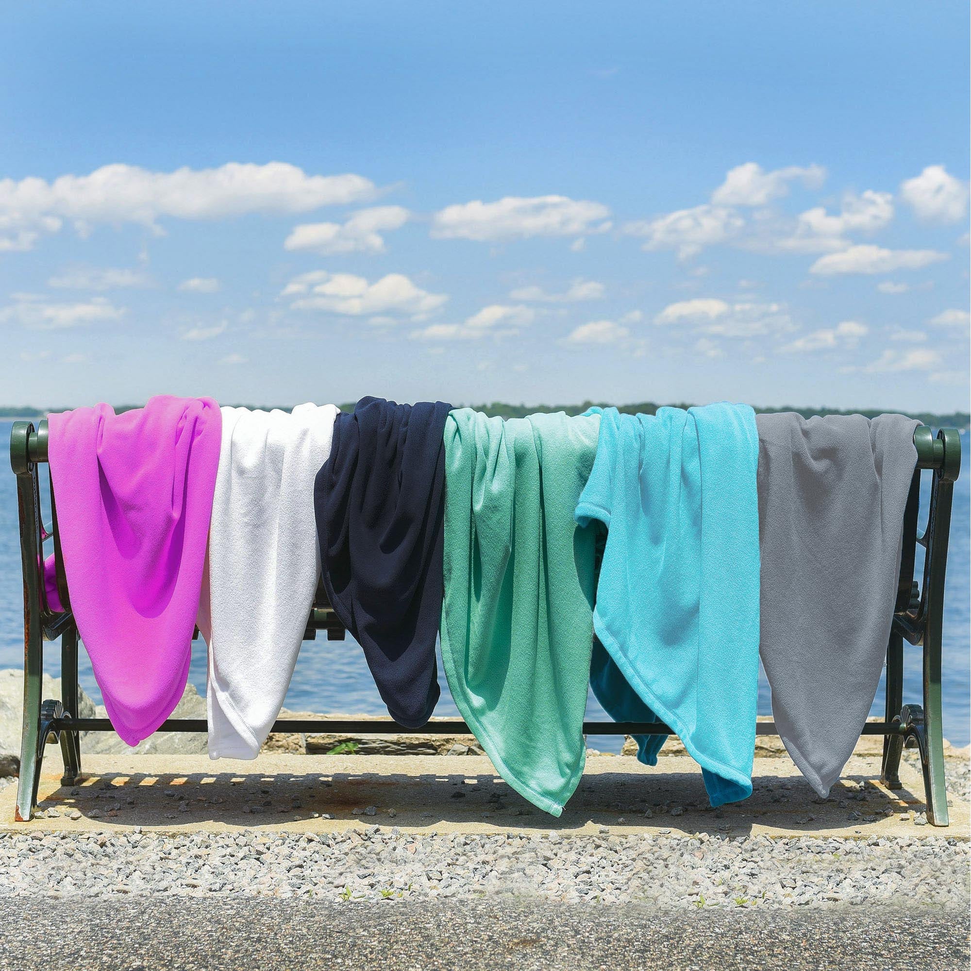 American Blanket Company - Peaceful Touch Fleece Throw Blankets - A selection of colorful fleece throws displayed on a rack outdoors, with vibrant colors including pink, white, navy, green, blue, and gray.