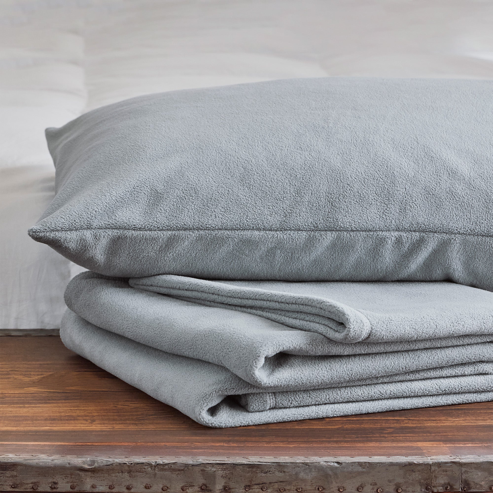American Blanket Company -  Folded light gray fleece blanket with a matching fleece pillow case on a wooden surface.
