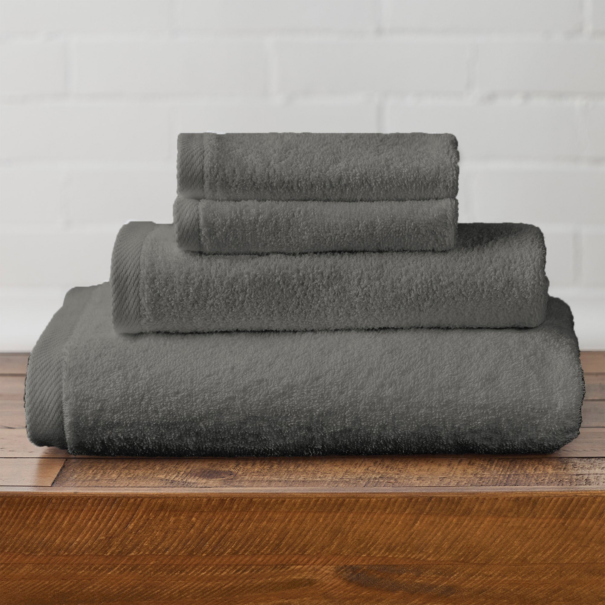 American Blanket Company -  Colorful 100% Cotton Towels - Stack of gray cotton towels on a wooden surface with a white brick wall background