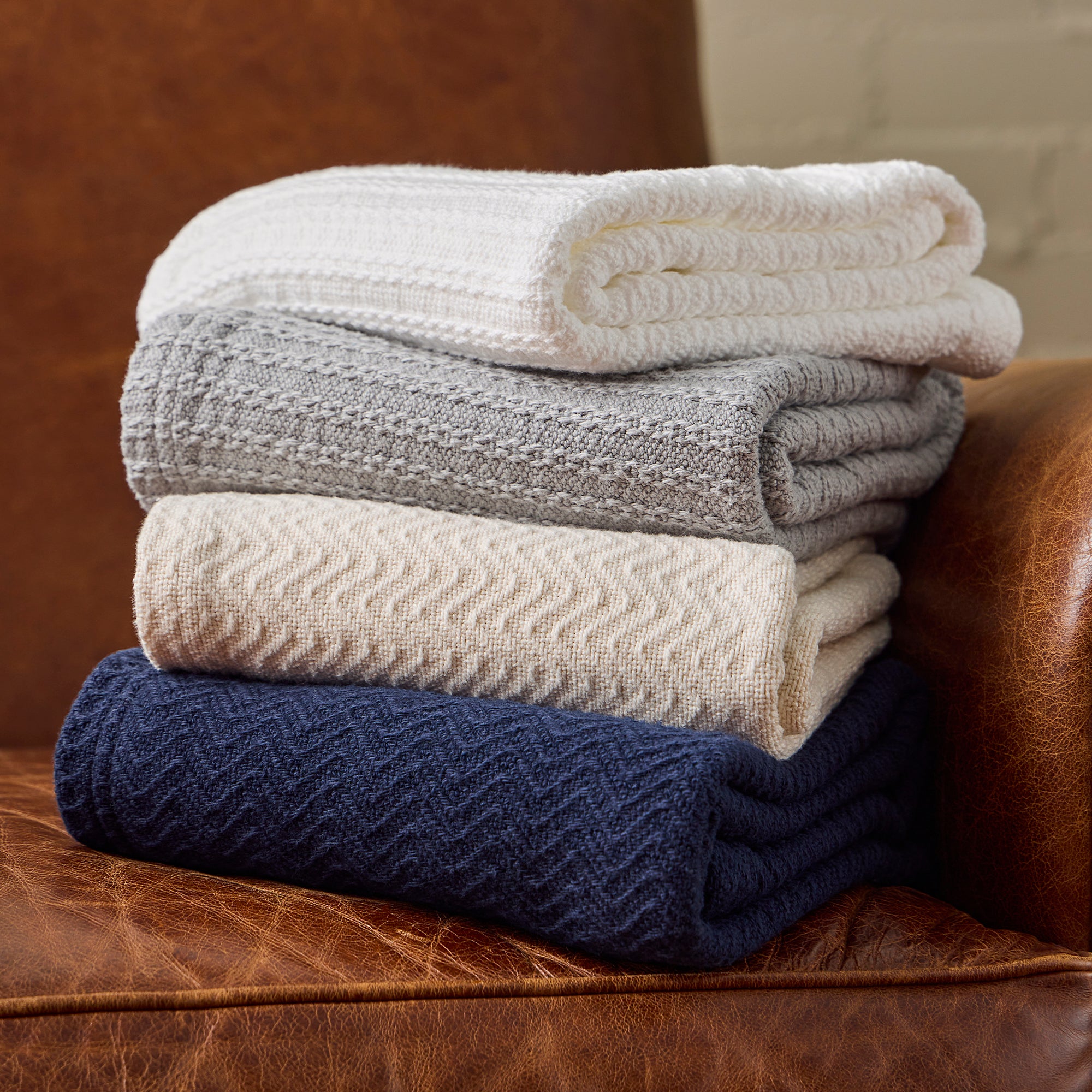 American Blanket Company - 100% Cotton Bedspread - Stacks of cotton bedspreads on a light leather arm chair.