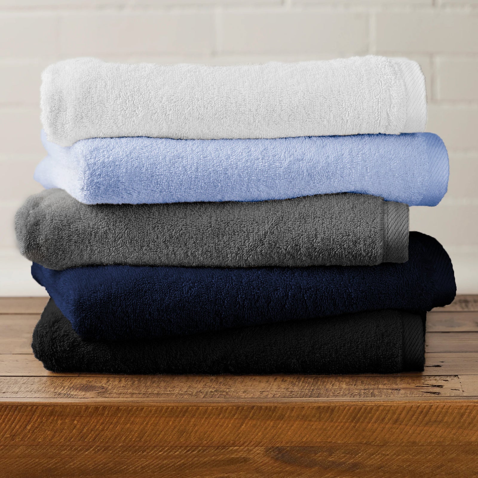 American Blanket Company -  Colorful Made in the USA 100% Cotton towels - Stack of folded towels in white, light blue, gray, navy, and black on a wooden surface with a neutral background.