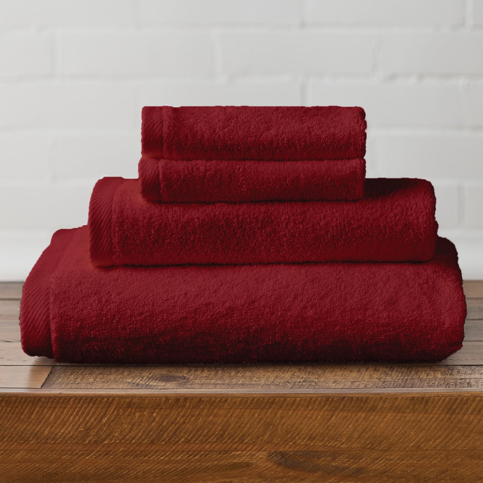 American Blanket Company -  Colorful 100% Cotton Towels - Set of red cotton towels stacked on a wooden surface with a white brick wall background