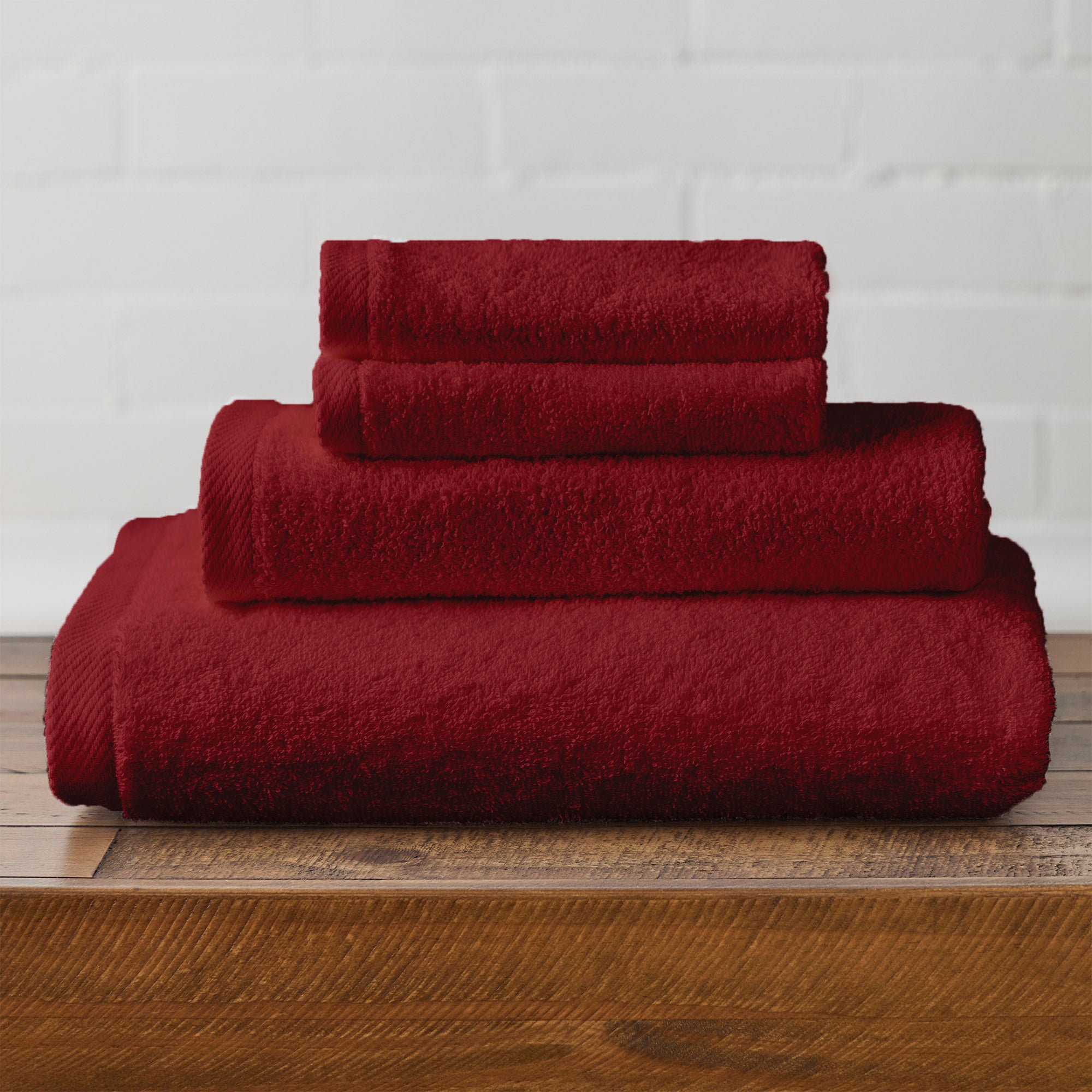 American Blanket Company -  Colorful 100% Cotton Towels - Set of red cotton towels stacked on a wooden surface with a white brick wall background