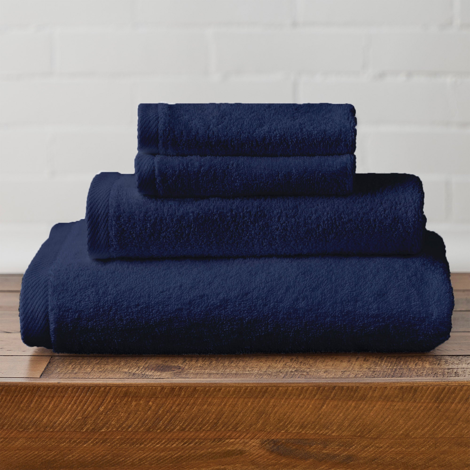 American Blanket Company -  Colorful 100% Cotton Towels - Stack of navy blue cotton towels on a wooden surface with a white brick wall background
