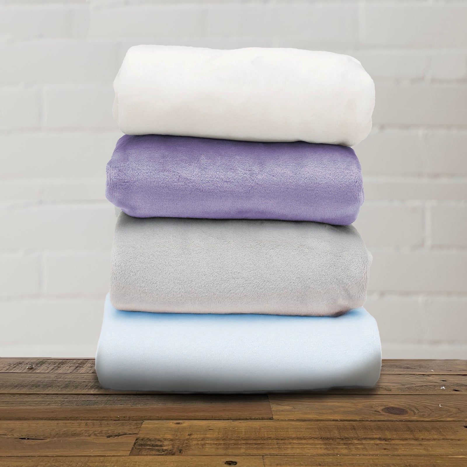 American Blanket Company - Luster Loft Fleece Blankets - Fleece Baby Blankets - A stack of folded fleece baby blankets in various solid colors including beige, purple, gray, and blue.