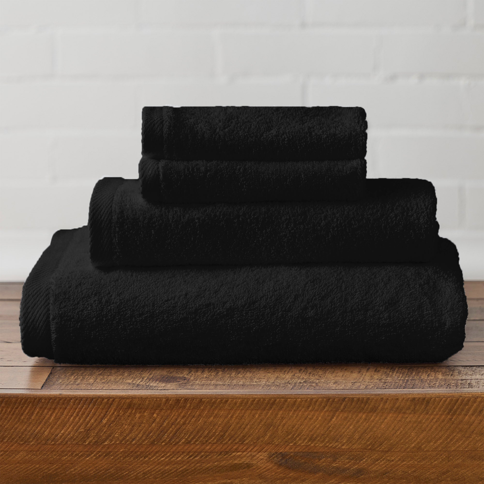 American Blanket Company -  Colorful 100% Cotton Towels - Set of black cotton towels on a wooden surface with a white brick wall background