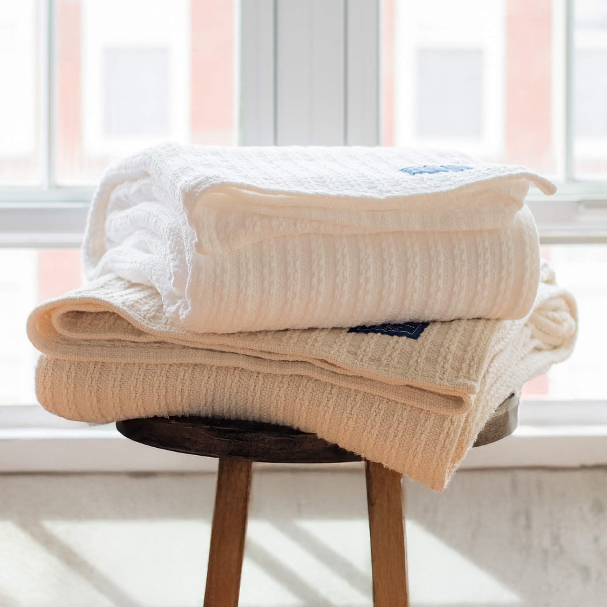 American Blanket Company - 100% Cotton Bedspread - Stack of cotton bedspreads on a wooden stool.