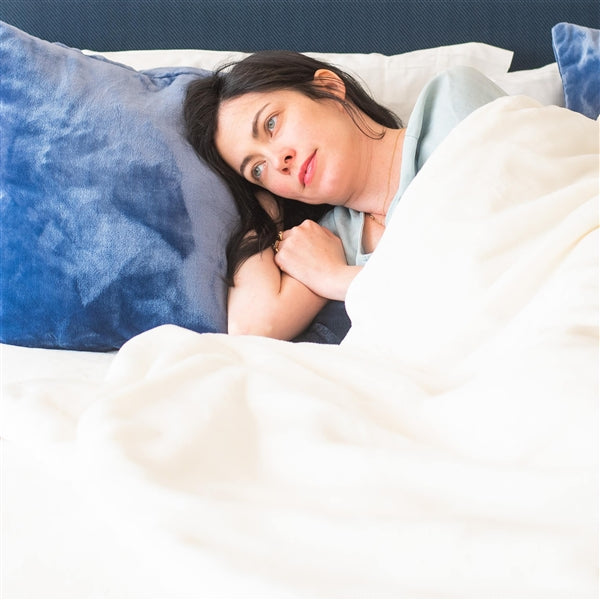 American Blanket Company - Luster loft weighted Fleece blanket - Pictured young woman relaxing under a luster loft weighted fleece blanket.