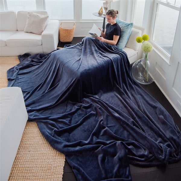 American Blanket Company - Luster Loft Oversized Fleece Blankets - Pictured young woman reading on a chaise lounge with an atlantic blue luster loft oversized blanket cascading across the room.