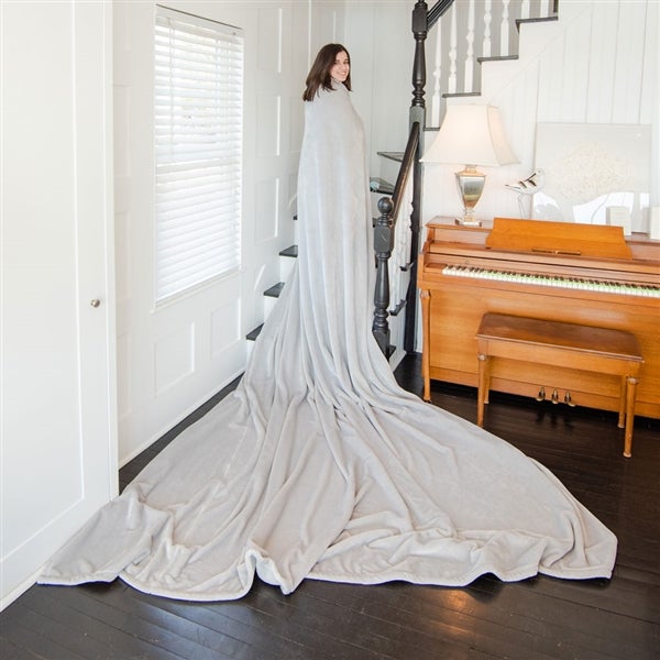 American Blanket Company - Luster Loft Oversized Fleece Blankets - pictured is a young woman smiling on a staircase while draped in a light gray luster loft oversized fleece blanket.