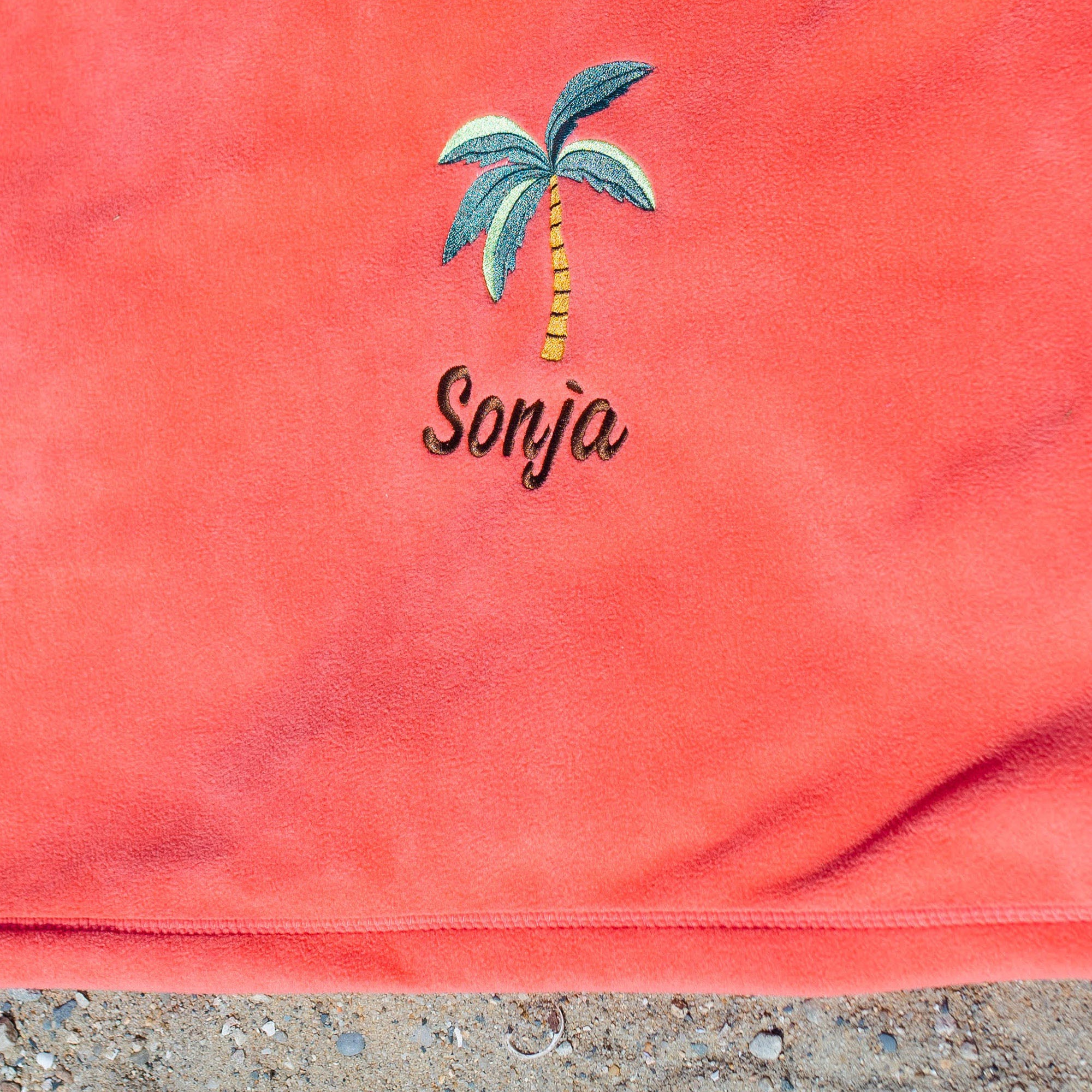 American Blanket Company - Peaceful Touch Beach Blankets - Pictured is a coral peaceful touch beach blanket with a palm tree embroidery 