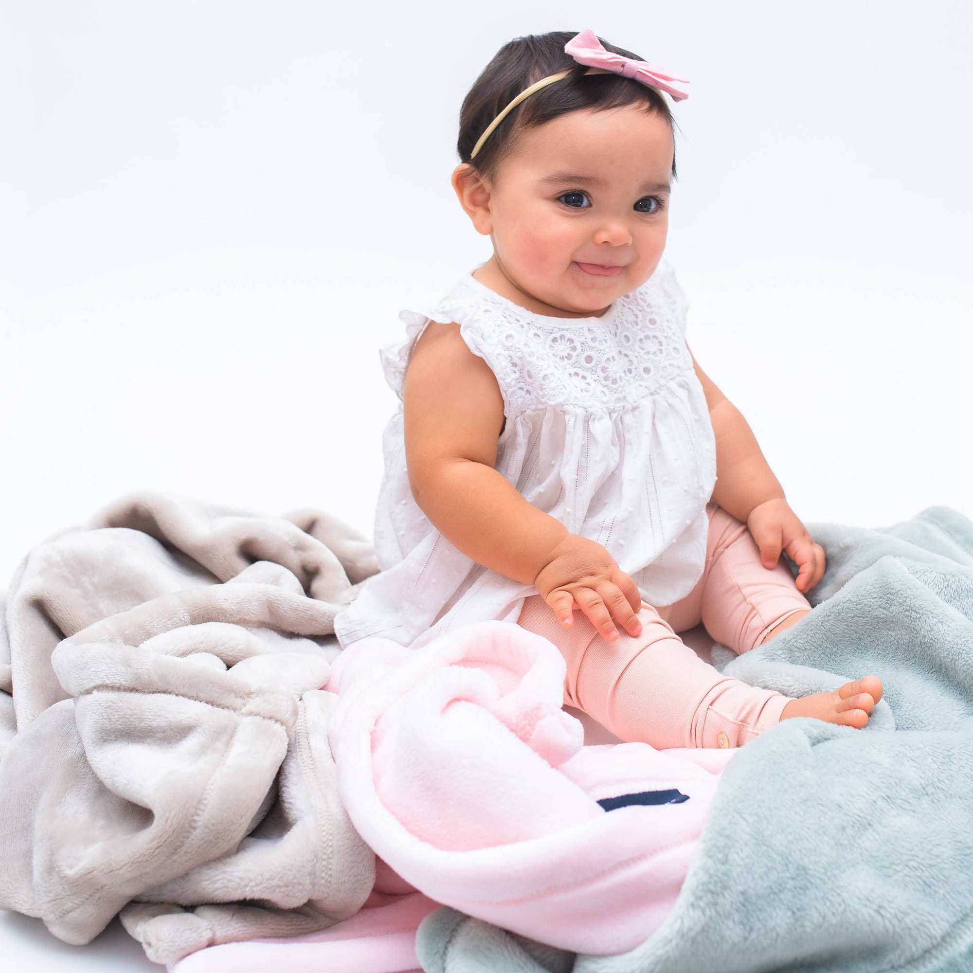 American Blanket Company - Luster Loft Fleece Blankets - Fleece Baby Blankets - A baby sitting on an assortment of fleece baby blankets