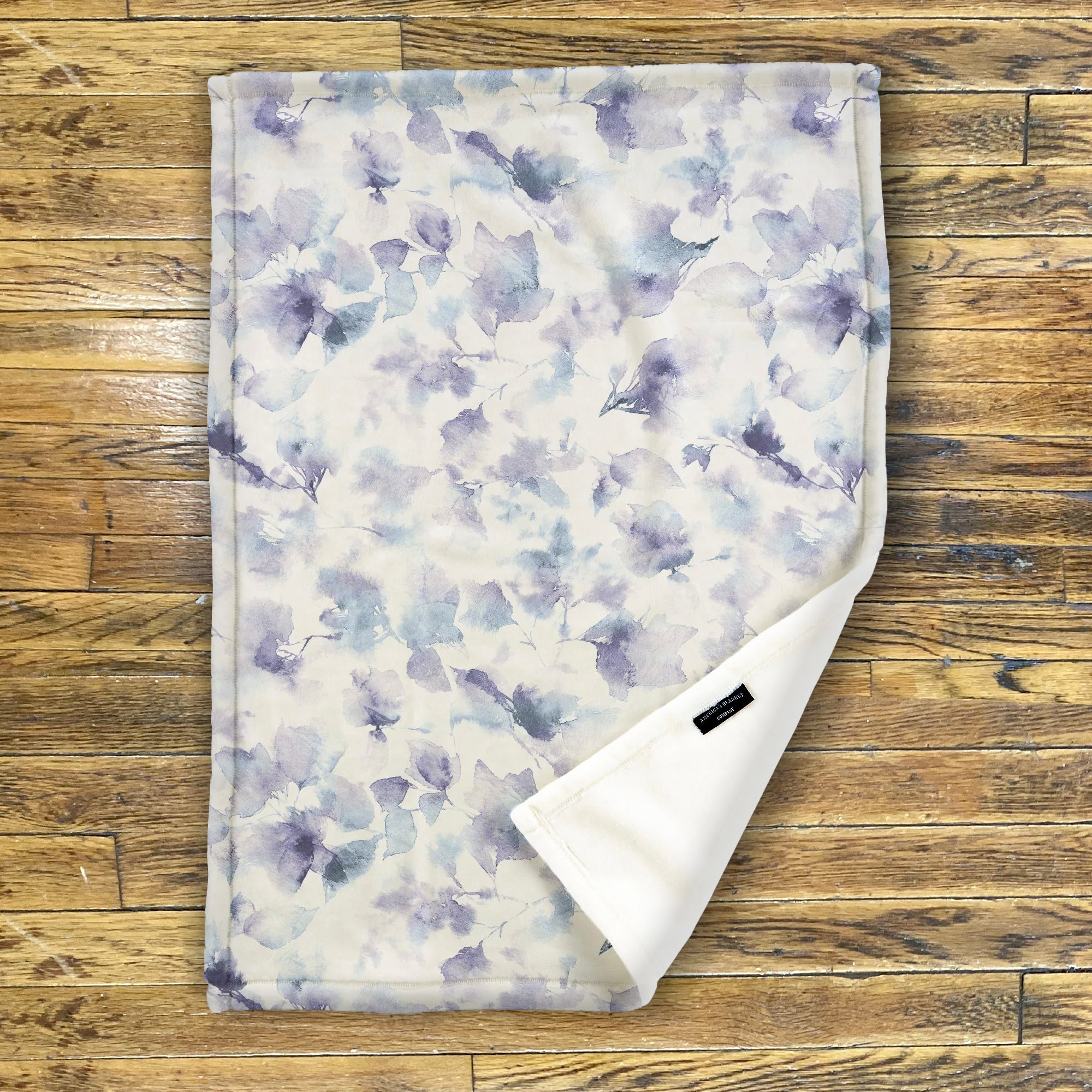 American Blanket Company - Luster Loft Fleece Blanket - Floral Printed Blankets Throws - a abstract floral pattern of blues on a white background and the fleece blanket on a wooden backdrop.
